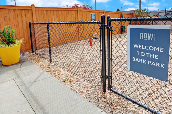 a rrw welcome to the bark park sign on a chain link fence