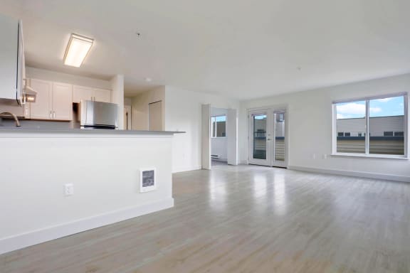 an empty living room with a kitchen and a large window