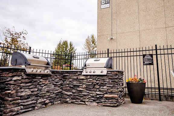 A stone wall with two BBQ grills on top and a black fence. at The Aviator, Renton, Washington