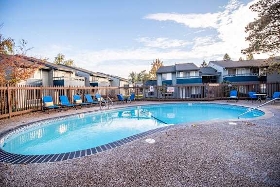 A swimming pool surrounded by a fence and chairs. at The Lakes at Fife, Fife, WA