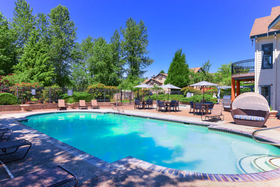 a swimming pool with chairs and umbrellas next to a house at Deer Creek Apartments, Puyallup
