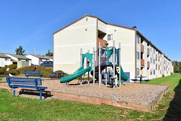 A playground with a green slide and a blue bench in front of a building. at The Verandas, Tacoma, WA, 98466