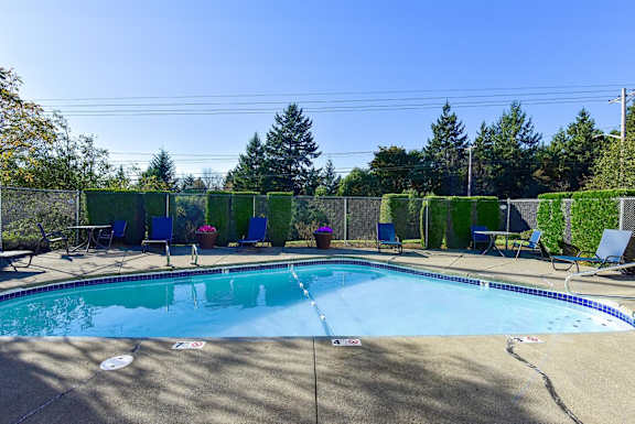 A pool surrounded by trees and chairs. at The Verandas, Tacoma, WA