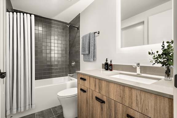 A modern bathroom with a white toilet, a wooden vanity, and a glass shower.