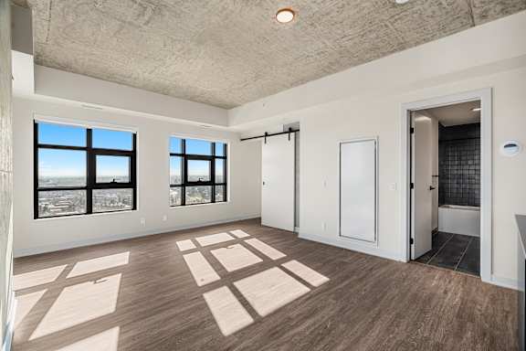 A spacious room with wooden flooring and large windows.