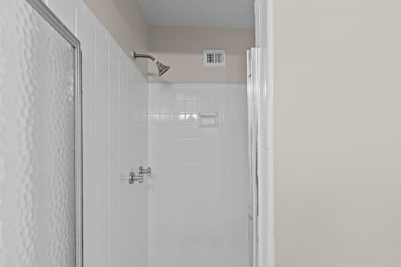 A white tiled shower with a silver faucet.