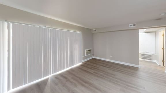 A room with a window covered by white blinds and a wooden floor.