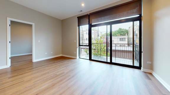A room with wooden floors and a sliding glass door leading to a balcony.