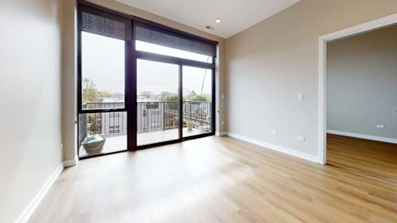 A room with a wooden floor and a sliding glass door leading to a balcony.