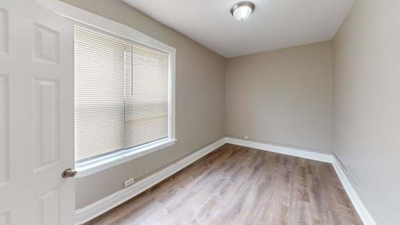 A room with a window covered by blinds and a wooden floor.