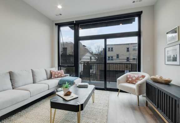 A living room with a grey couch, a black coffee table, and a chair with a red pillow.