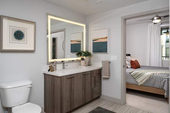 A bathroom with a toilet, sink, mirror, and bed.