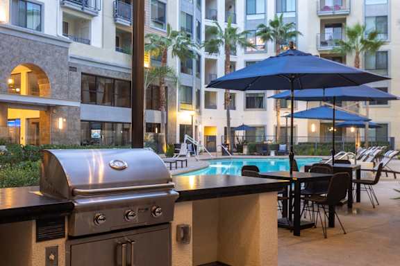 A BBQ grill is in the foreground of a poolside patio.