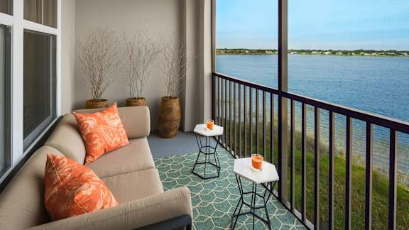 A balcony with a couch, pillows, and a table with a candle on it.