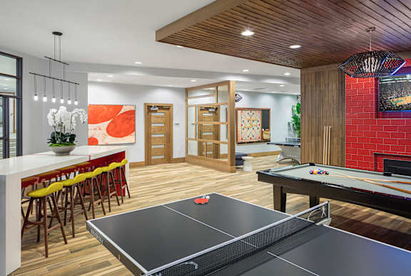 A ping pong table is in the middle of a room with a bar and a pool table.