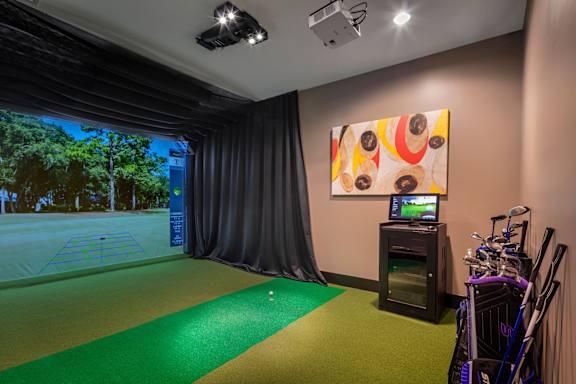 A room with a golf simulator and a painting on the wall.