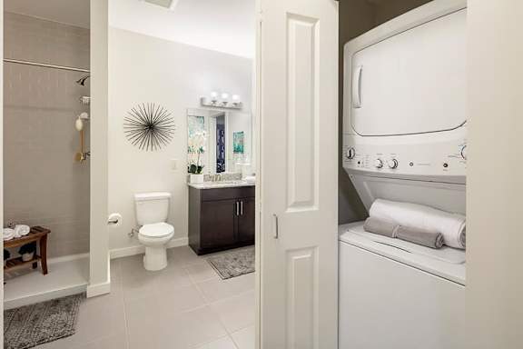 A white washing machine is in a bathroom with a toilet and sink.
