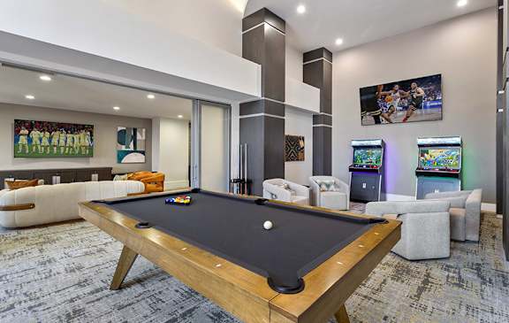 A pool table is in the middle of a room with a TV and arcade games.