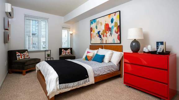 A bedroom with a bed, a red dresser, and a painting on the wall.