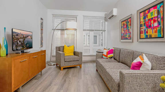 A living room with a grey couch, a yellow pillow on the chair and a painting on the wall.