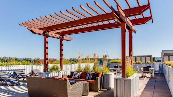 A red pergola is over a patio with couches and tables.