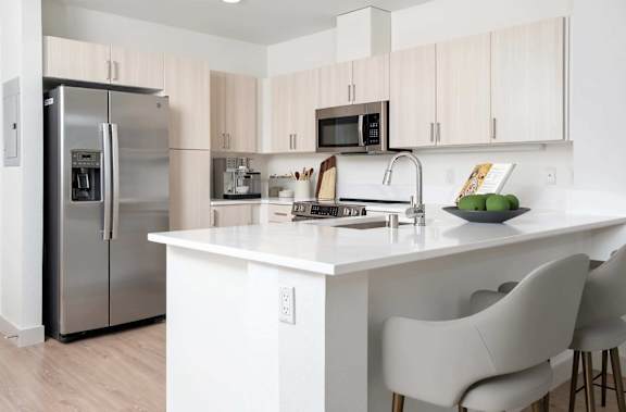A kitchen with a white counter top and white chairs.