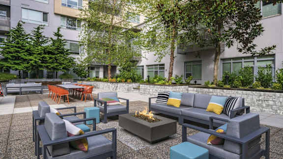 A modern outdoor seating area with grey couches and a fire pit.