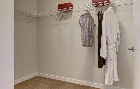 A white closet with clothes hanging on a rod.