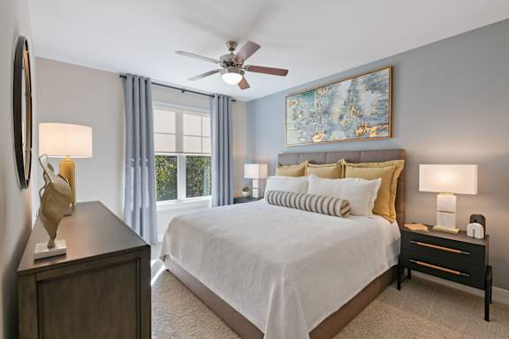 A bedroom with a large bed, a ceiling fan, and a painting on the wall.