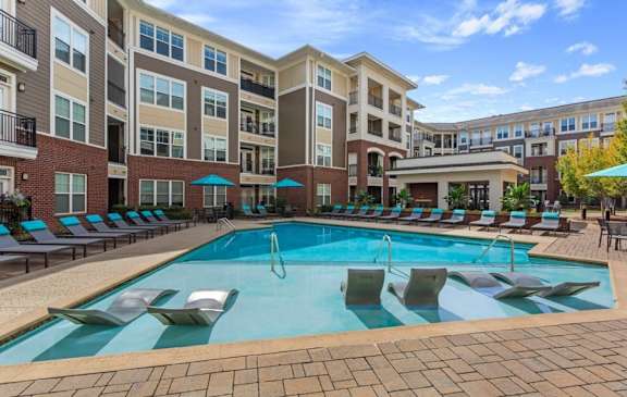 A large swimming pool surrounded by lounge chairs in front of apartment buildings.