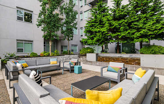 A patio with a grey couch and a black table.