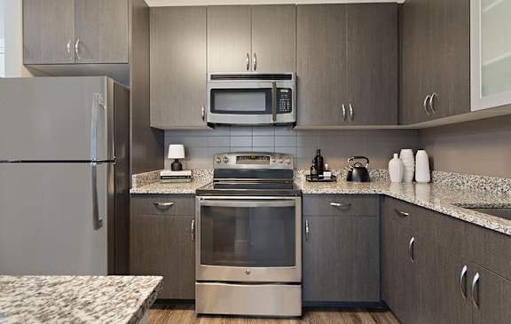 A modern kitchen with a stainless steel refrigerator, microwave, oven, and cabinets.