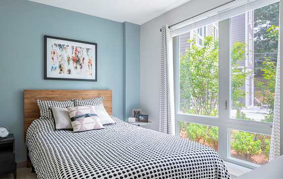 A bedroom with a bed, nightstand, window, and a picture on the wall.