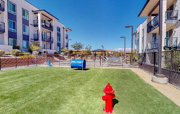 A red fire hydrant sits in the middle of a grassy area in front of apartment buildings.