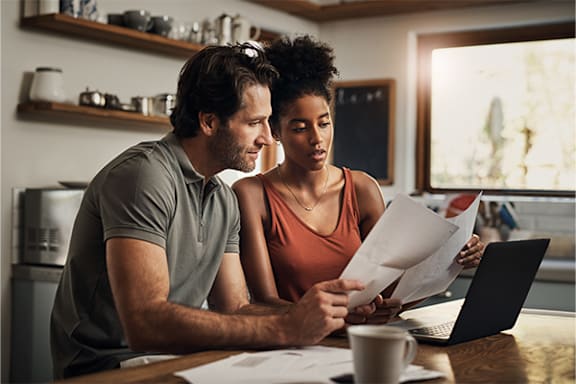 A man and woman are sitting at a table looking at papers and a laptop.