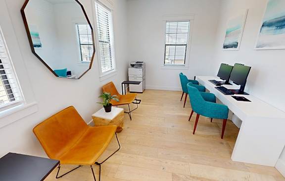 A room with a desk, chairs and a mirror.