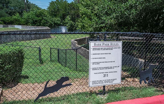 A sign in front of a fence that says Bark Park Rules.