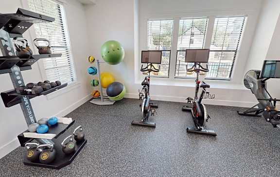 A gym with a variety of equipment including weights, exercise balls, and stationary bikes.