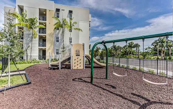 A playground with a slide and swings in front of a building.