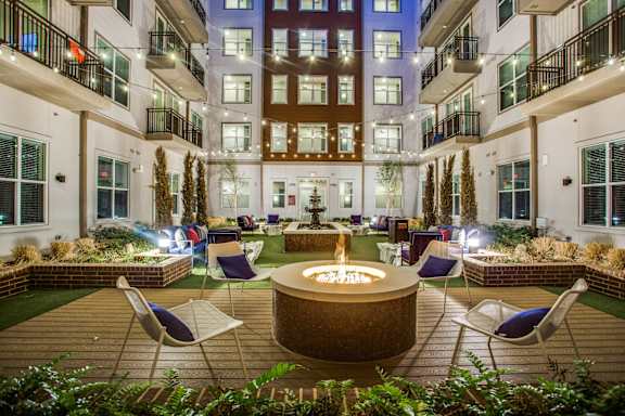 A courtyard with a fire pit surrounded by chairs and plants.