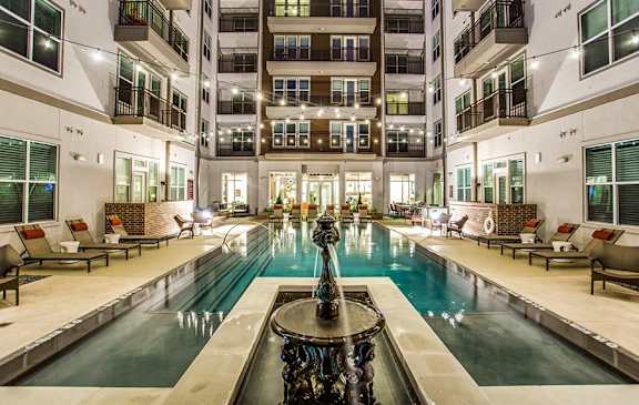 A large fountain in the middle of a pool surrounded by lounge chairs.