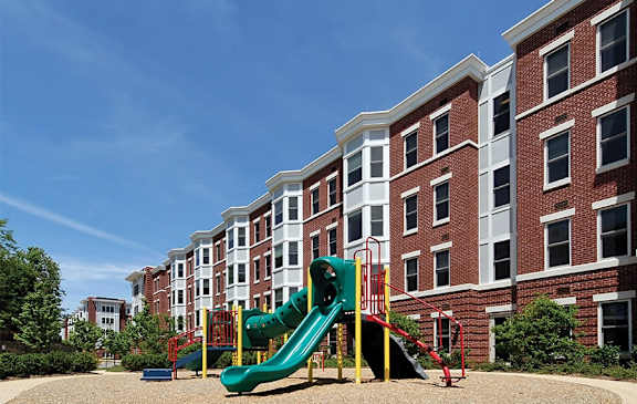 A playground with a green slide in front of a red brick building.