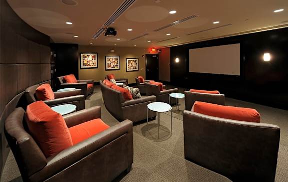A room with a screen and chairs with orange cushions.