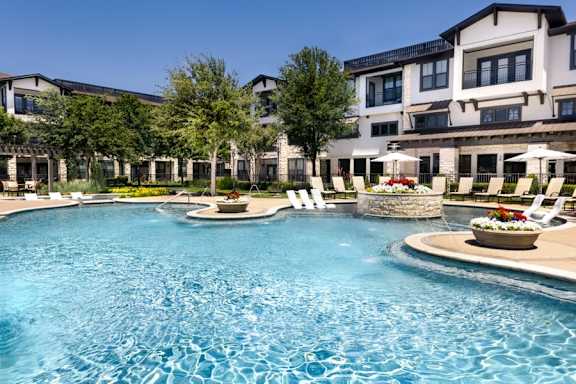 A large swimming pool in front of a building with a fountain in the middle.