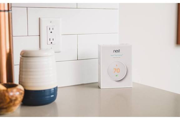 A Nest thermostat is on a table next to a ceramic vase.