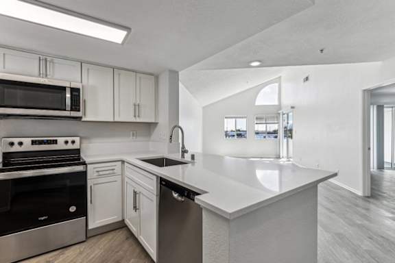 A modern kitchen with a stainless steel oven and microwave, white cabinets, and a large island with a sink.