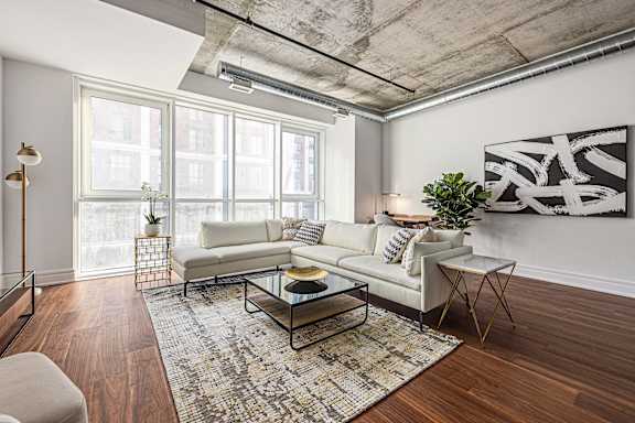 A living room with a white couch, a glass coffee table, and a large abstract painting on the wall.