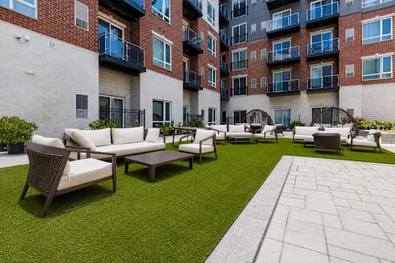 A patio area with a white couch and a green lawn.