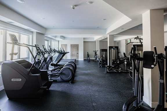 A gym with a row of treadmills and elliptical machines.