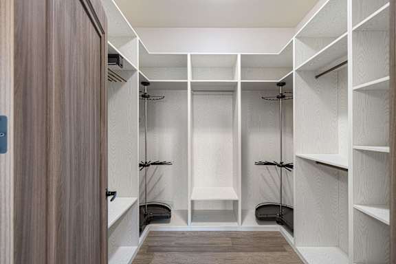 A walk-in closet with white shelving and a wooden floor.